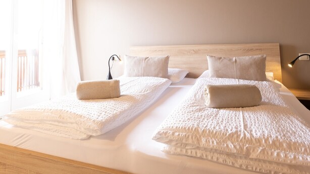 Una cama grande con cabecera de madera, sábanas blancas y una mesita de noche con lámpara.