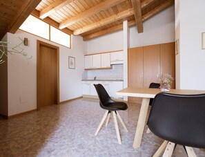A modern kitchen with white cabinets, a wooden ceiling, and a dining area with a table and chairs.