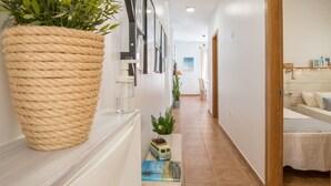 A hallway with a large potted plant, framed pictures on the wall, a small table with a toy car and a book, and a bed in the background. - Maritime Holiday Home Casa Yerida with Pool and Wi-Fi (Cotillo)