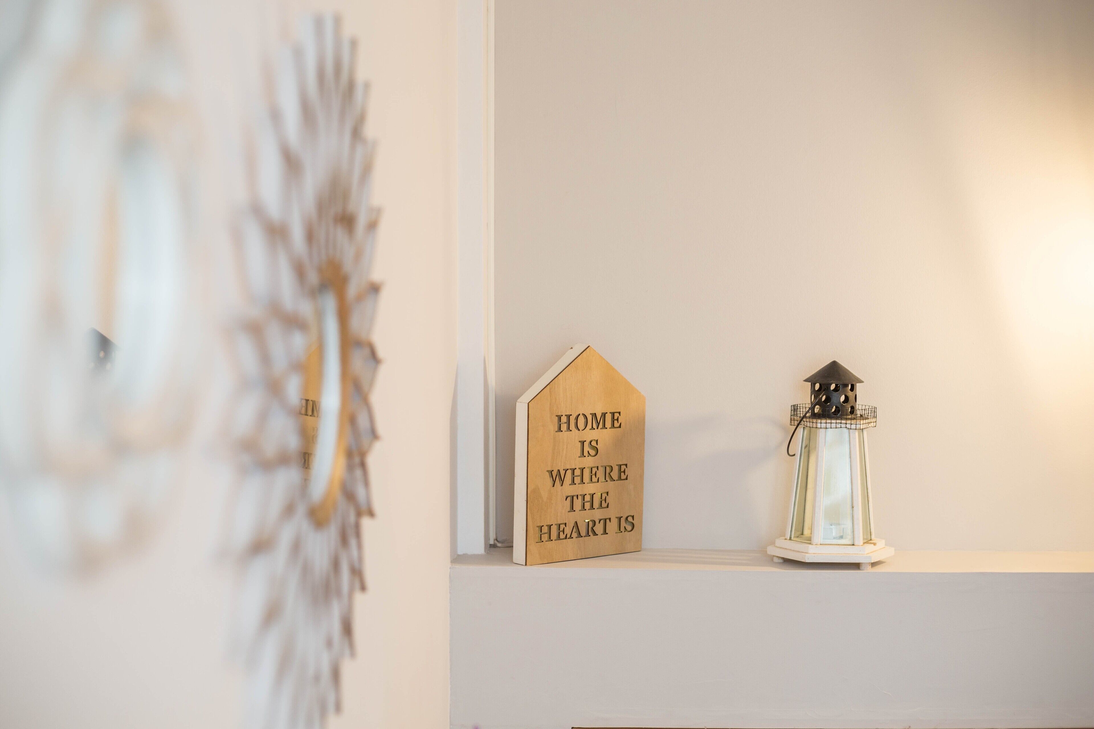 Een muur met een houten bord waarop staat 'HOME IS WHERE THE HEART IS' en een witte lantaarn.