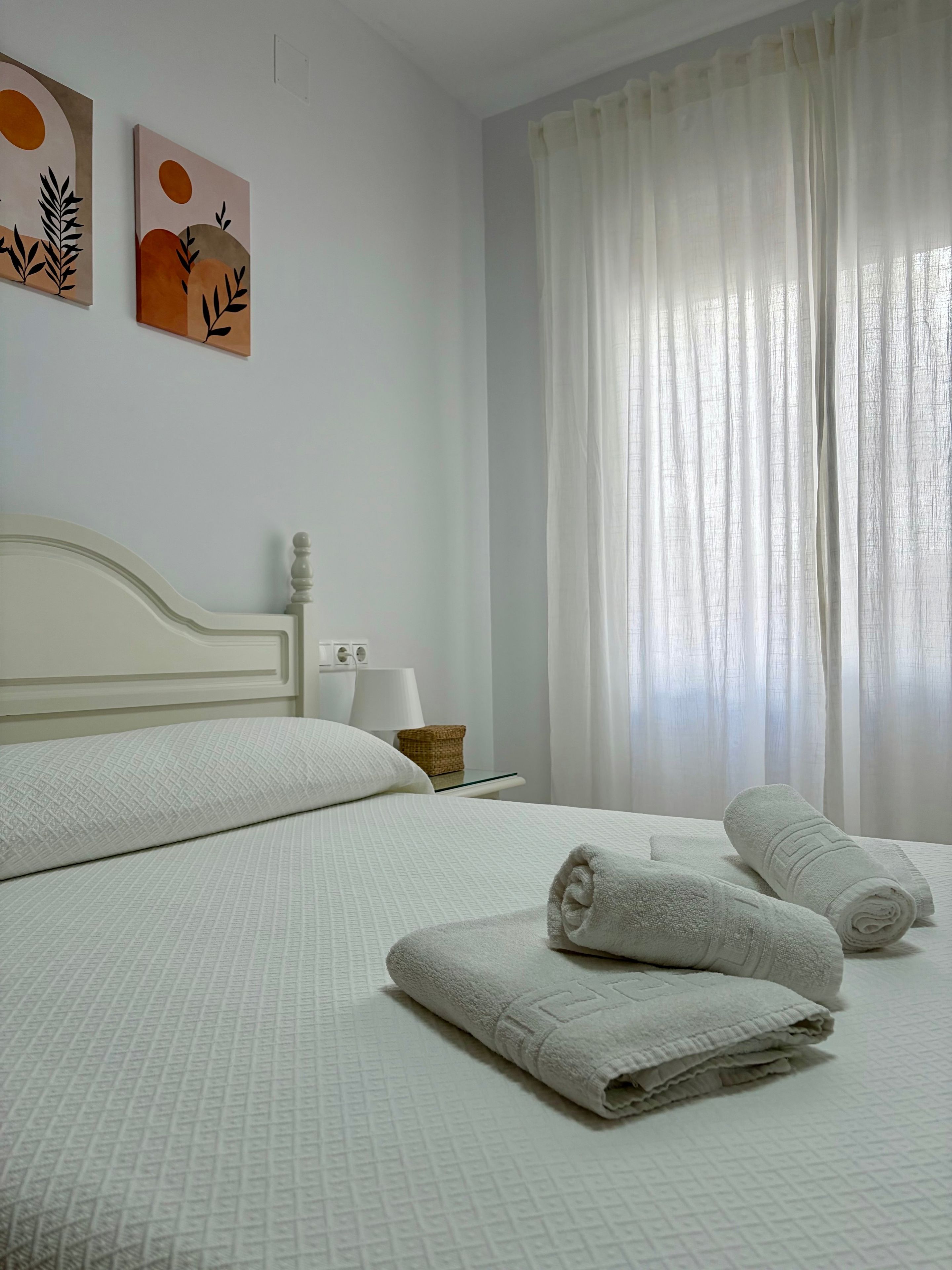 Habitación de hotel con una cama, dos almohadas, una mesita de noche con una lámpara, una cesta y dos toallas.