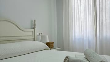 Habitación de hotel con una cama, dos almohadas, una mesita de noche con una lámpara, una cesta y dos toallas.