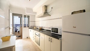 A kitchen with white cabinets, a microwave, a stove, and a refrigerator. - Newly Renovated Apartment “Conil Centro” with Wi-Fi, Terrace & Air Conditioning; Parking Available (Conil de la Frontera)