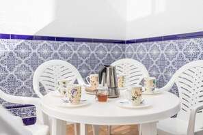 A white table with floral-patterned cups and saucers, a silver coffee pot, and a small jar of honey.