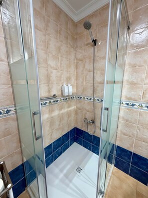 A glass-enclosed shower stall with beige and blue tiles, a handheld showerhead, and a wall-mounted faucet.