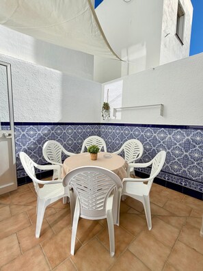 A dining area with a round table and white chairs, a hanging plant, and a blue and white patterned wall.