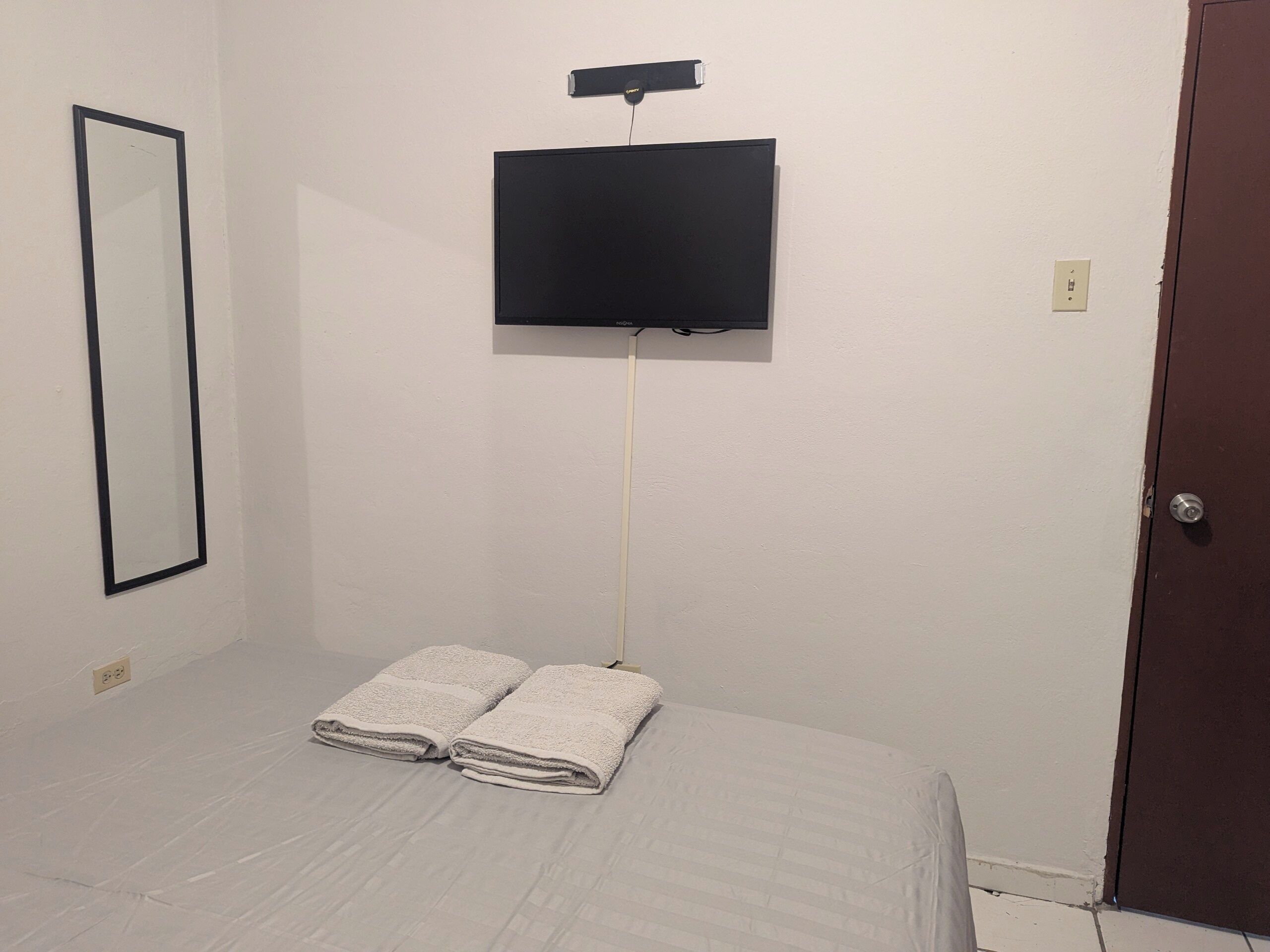 Una habitación con una cama, un televisor en la pared y una puerta.