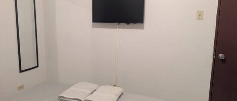 Una habitación con una cama, un televisor en la pared y una puerta.