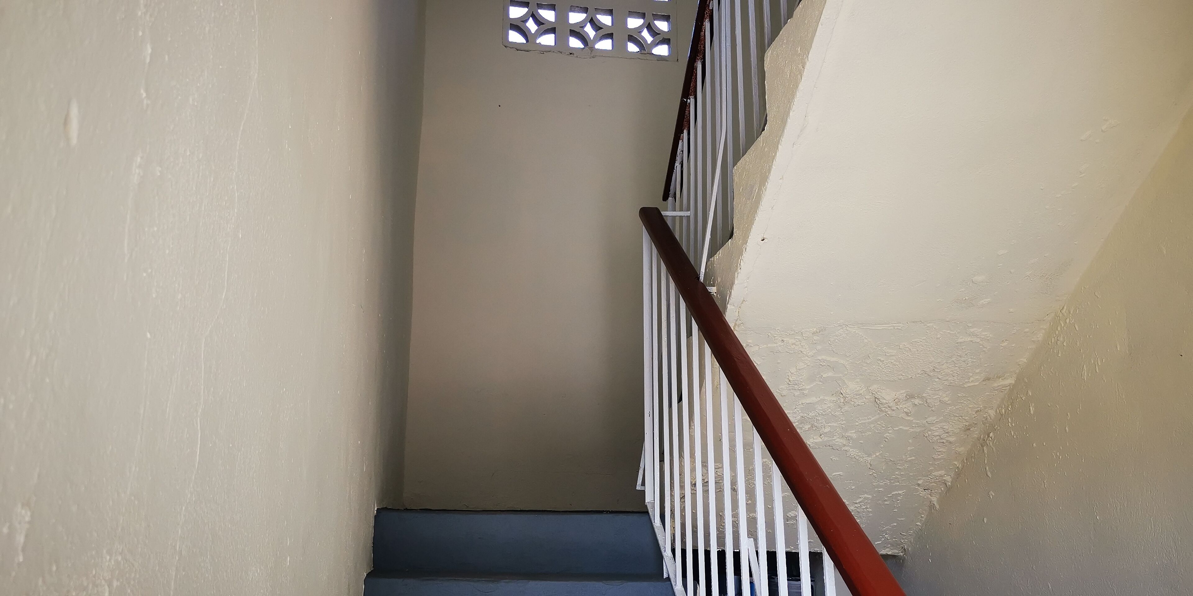 Un escalier avec des rampes blanches et une main courante rouge, qui monte.