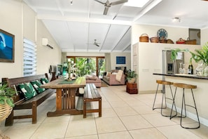 A spacious living area with a wooden dining table, a sofa, and a kitchen area with a refrigerator and bar stools. - Luxurious Family Villa with Private Pool, Nestled in Cairns` Tropical Paradise (Whitfield)