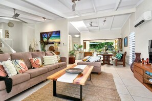 A modern living room with a sofa, coffee table, and a dining area with chairs. - Luxurious Family Villa with Private Pool, Nestled in Cairns` Tropical Paradise (Whitfield)