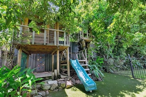 A wooden playhouse with a slide, surrounded by lush greenery. - Luxurious Family Villa with Private Pool, Nestled in Cairns` Tropical Paradise (Whitfield)