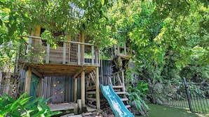 A wooden playhouse with a slide and climbing wall, surrounded by lush greenery. - Luxurious Family Villa with Private Pool, Nestled in Cairns' Tropical Paradise (Whitfield)