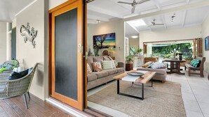 A spacious living room with a sliding glass door leading to a balcony, a sofa set, a coffee table, and a dining area with a table and chairs. - Luxurious Family Villa with Private Pool, Nestled in Cairns' Tropical Paradise (Whitfield)