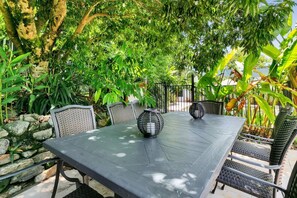 An outdoor patio with a table and chairs, surrounded by lush greenery and a stone wall.