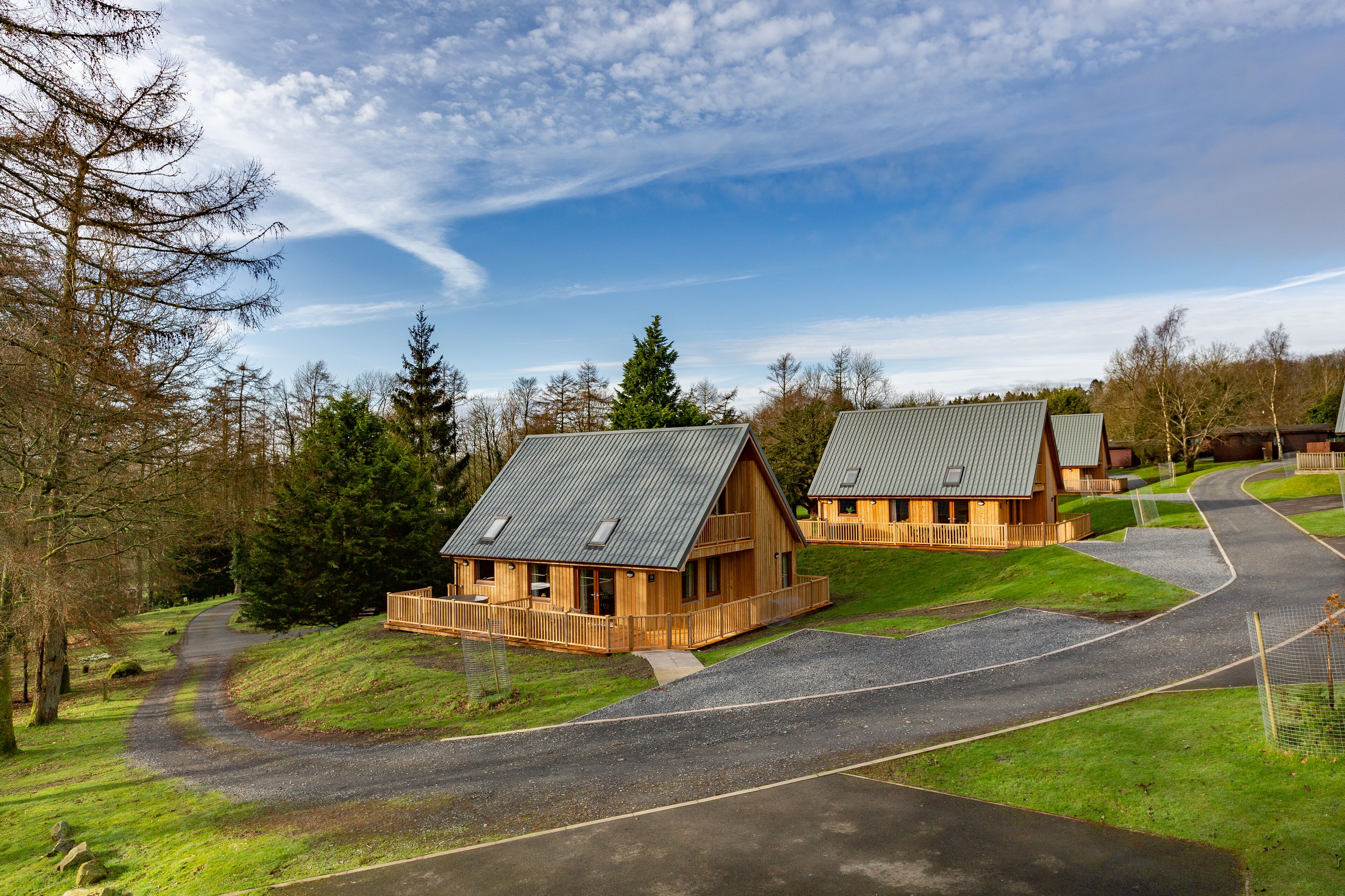 A row of wooden cabins with sloped roofs, surrounded by a gravel driveway and grassy areas.