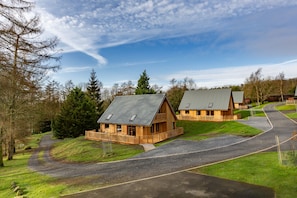 A row of wooden cabins with sloped roofs, surrounded by a gravel driveway and grassy areas.