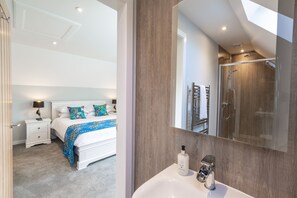 A modern bedroom with a large bed, bedside tables, a nightstand, and a bathroom with a shower and sink.