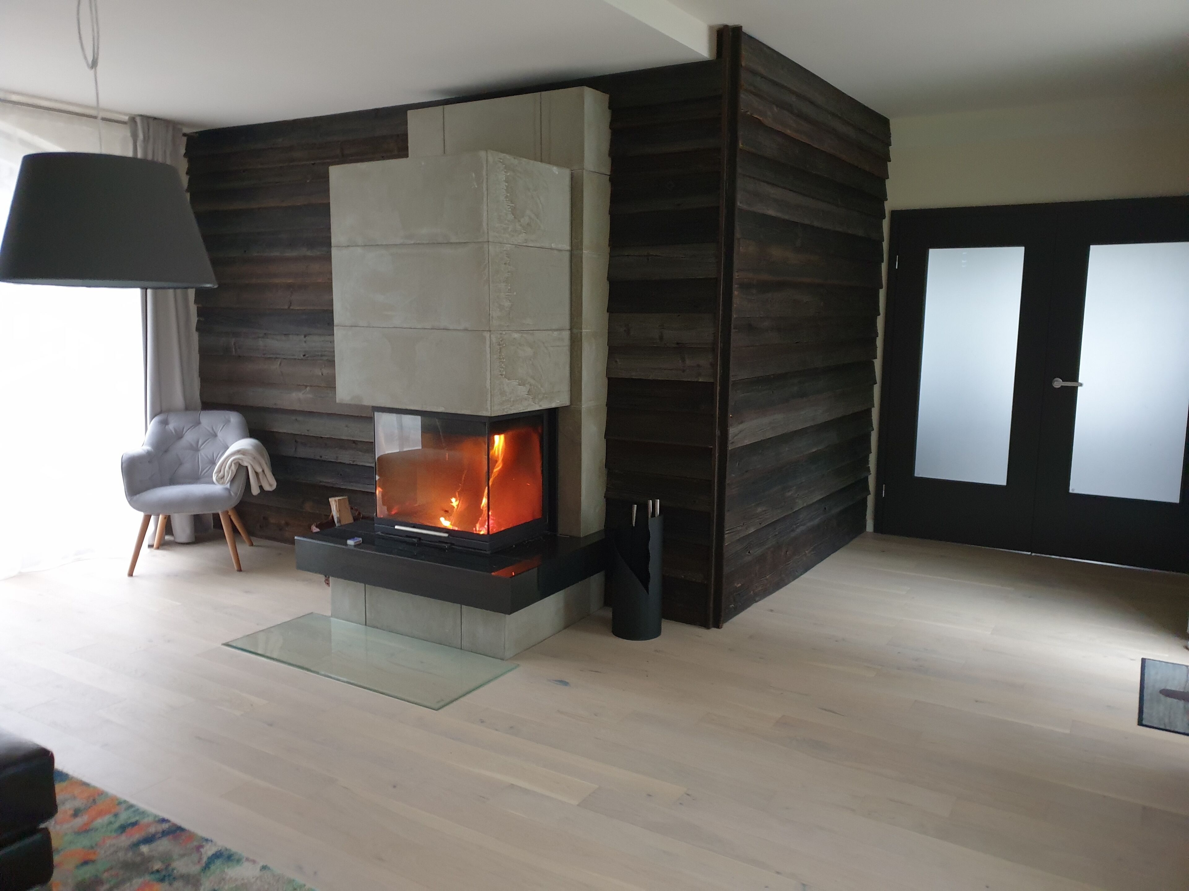 A modern living room with a fireplace, a grey armchair, and a glass coffee table.