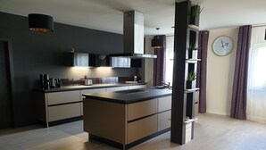 A modern kitchen with a central island, dark cabinetry, and pendant lighting. - Vacation home for 20 people, fireplace, sauna, 10 rooms, 10 bathrooms, very large, distant view (Altenberg)
