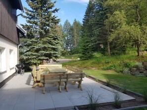 A patio with a wooden table and benches, surrounded by trees and a house. - Vacation home for 20 people, fireplace, sauna, 10 rooms, 10 bathrooms, very large, distant view (Altenberg)