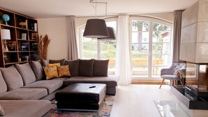 A modern living room with a sectional sofa, a glass coffee table, and a bookshelf. - Vacation home for 20 people, fireplace, sauna, 10 rooms, 10 bathrooms, very large, distant view (Altenberg)
