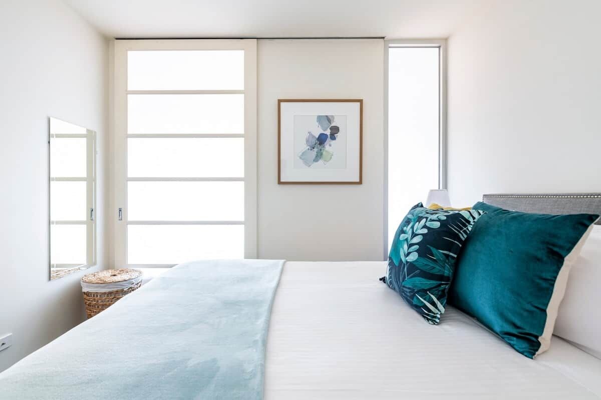A bedroom with a bed, pillows, a framed artwork, and a window.