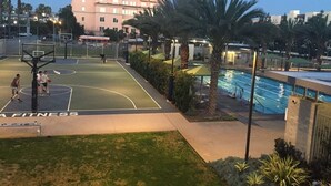 An outdoor basketball court adjacent to a swimming pool, surrounded by palm trees and a building in the background. - Silicon Beach Escape (Los Angeles)