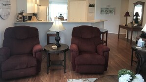 A living room with two armchairs, a small table with a lamp, and a kitchen area in the background. - Hillside Hideaway ~ Spacious Poolside 2 bed 2 bath condo (Branson)