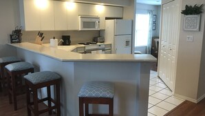 A kitchen with a central island, bar stools, a microwave, a refrigerator, and a coffee maker. - Hillside Hideaway ~ Spacious Poolside 2 bed 2 bath condo (Branson)