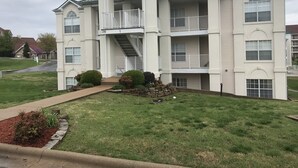 A multi-story residential building with a central staircase, balconies, and a well-maintained lawn. - Hillside Hideaway ~ Spacious Poolside 2 bed 2 bath condo (Branson)