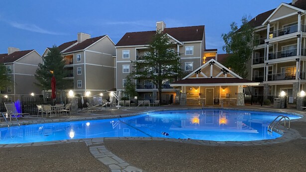 A swimming pool surrounded by stone-tiled walkways, with lounge chairs and umbrellas. - Hillside Hideaway ~ Spacious Poolside 2 bed 2 bath condo (Branson)