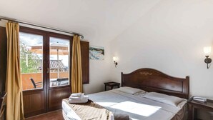 Ein Hotelzimmer mit Bett, Vorhängen, einem Gemälde, einem Nachttisch und Blick nach außen.