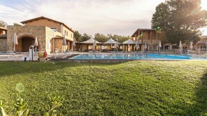 Ein Poolbereich mit Liegestühlen und Sonnenschirmen, umgeben von Steinbauten und einem großen Baum.