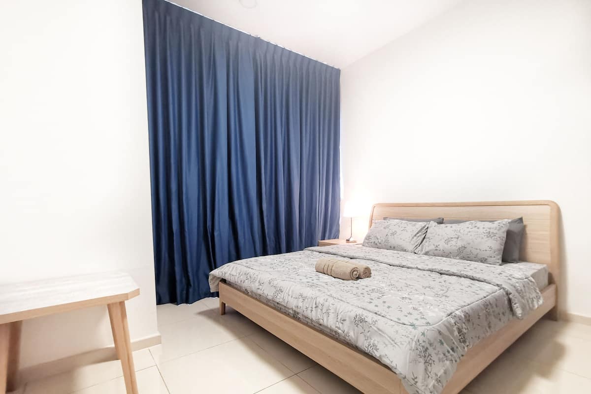 A bedroom with a bed, a nightstand, a desk, and a large window with blue curtains.