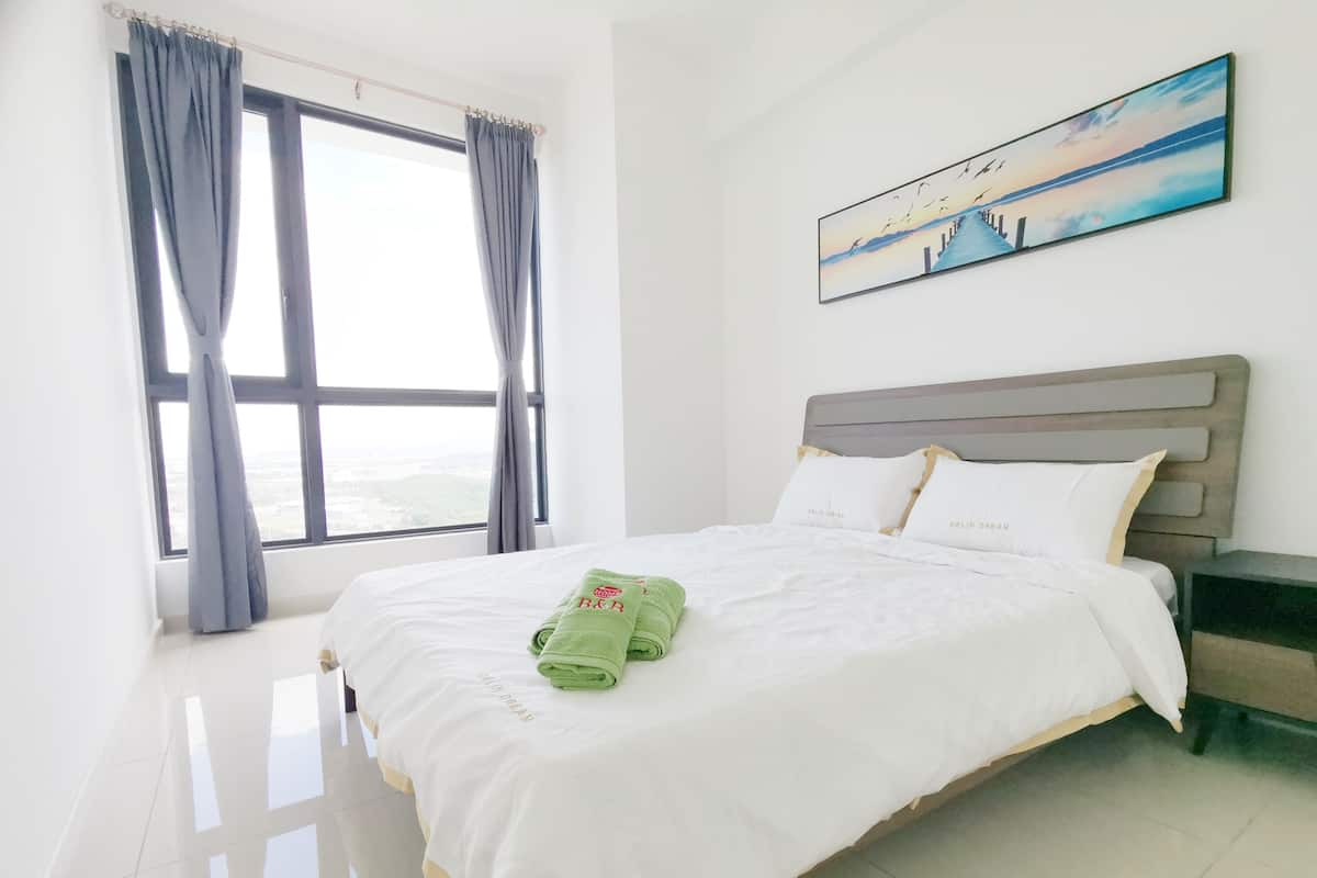 A hotel room with a large bed, a view through the window, and a painting on the wall.