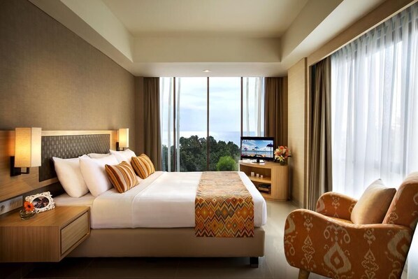Ein Hotelzimmer mit einem großen Bett, einem Fernseher, einem Schreibtisch und Blick ins Freie.
