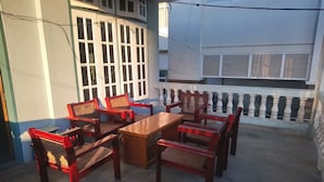 A covered outdoor seating area with a wooden table and chairs, a white railing, and a window with blinds. - Diamond Star Guest House (Nyaungshwe)