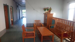 A room with a wooden bench, a table, and chairs. There is a cabinet with flowers on top. The room has a wooden floor and a window. - Diamond Star Guest House (Nyaungshwe)