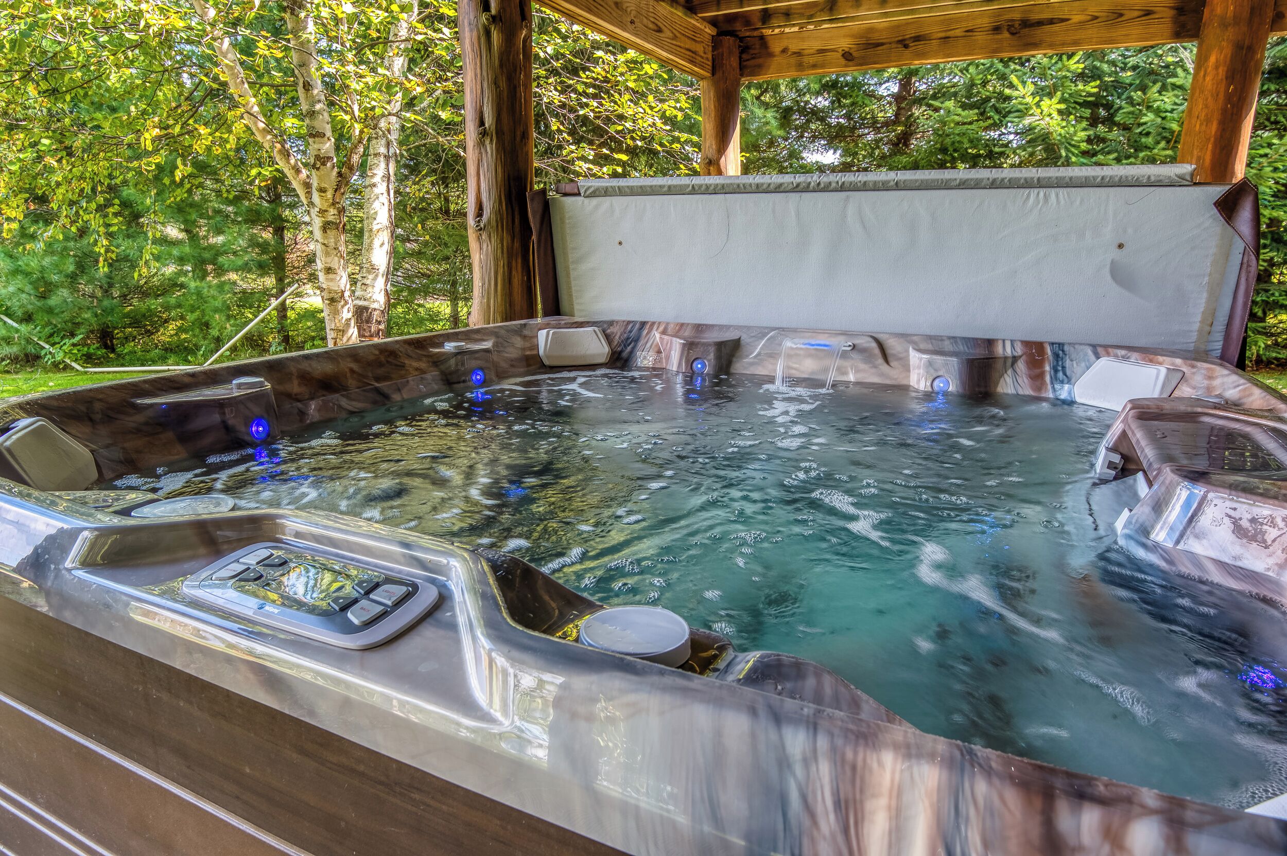 Un jacuzzi con cubierta de madera y un toldo, rodeado de árboles.