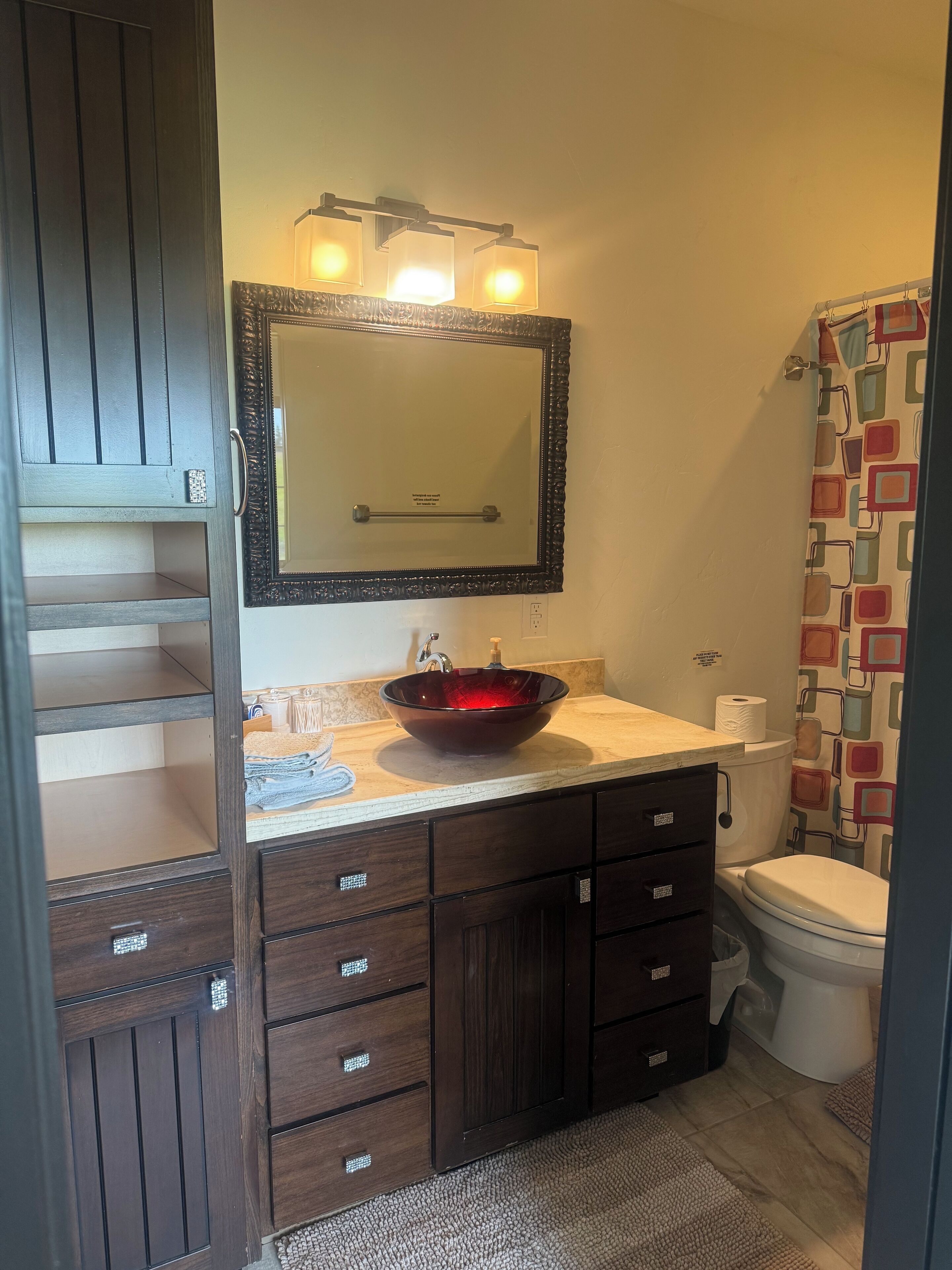 A bathroom with a dark wood vanity, a large mirror, a glass bowl sink, and a toilet.