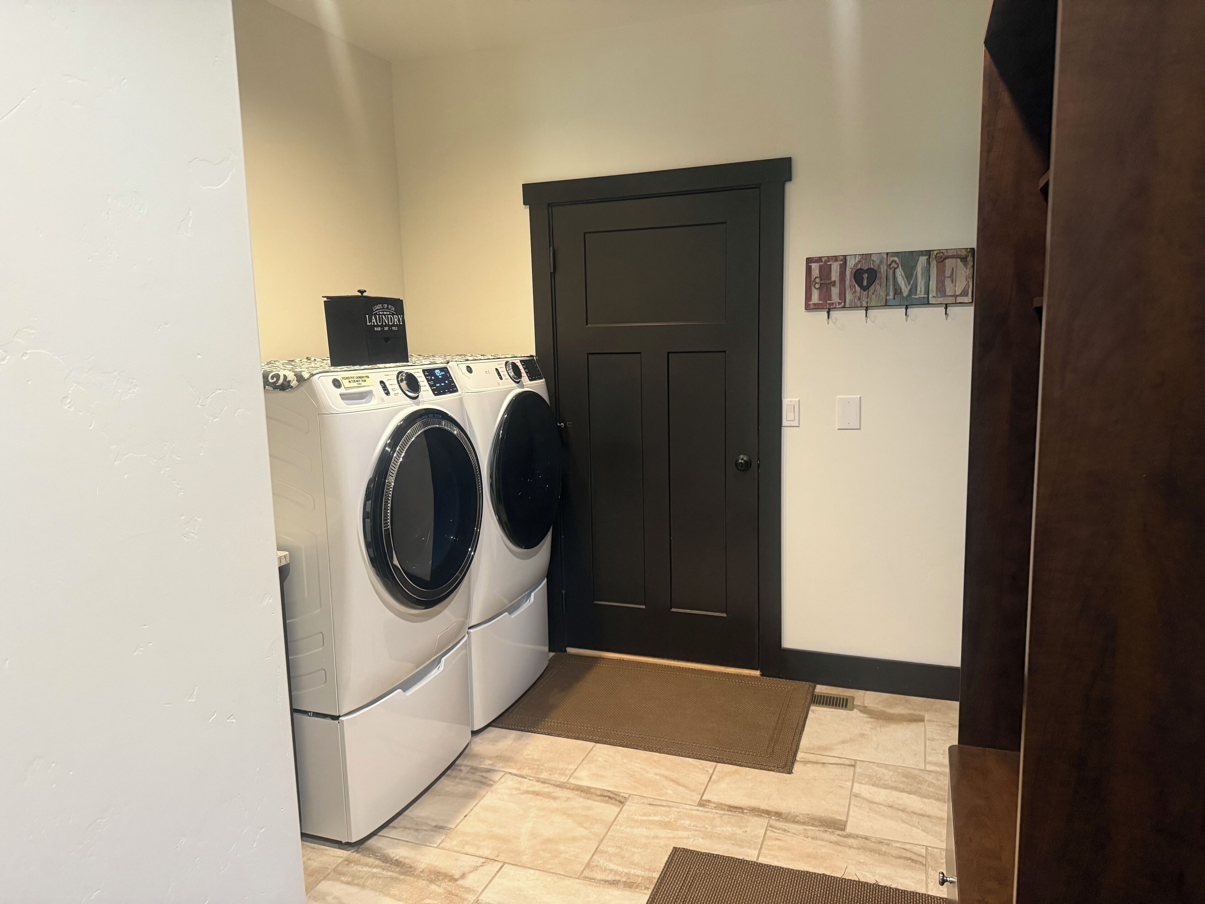 A laundry room with two front-loading washers and dryers, a dark door, and a small rug on the floor.