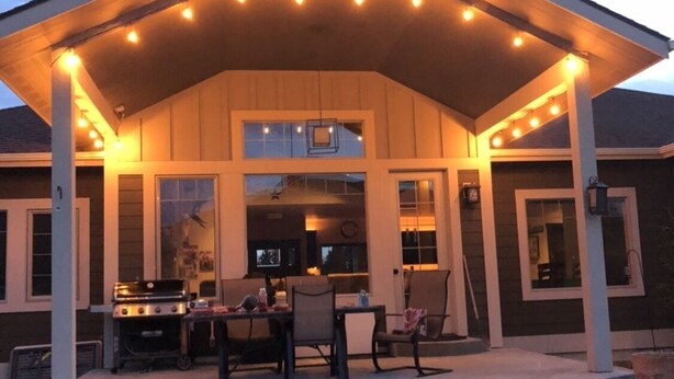 A covered outdoor patio with a grill and seating area, large windows, and a well-lit ambiance. - Country setting close to Glacier National Park (Columbia Falls)