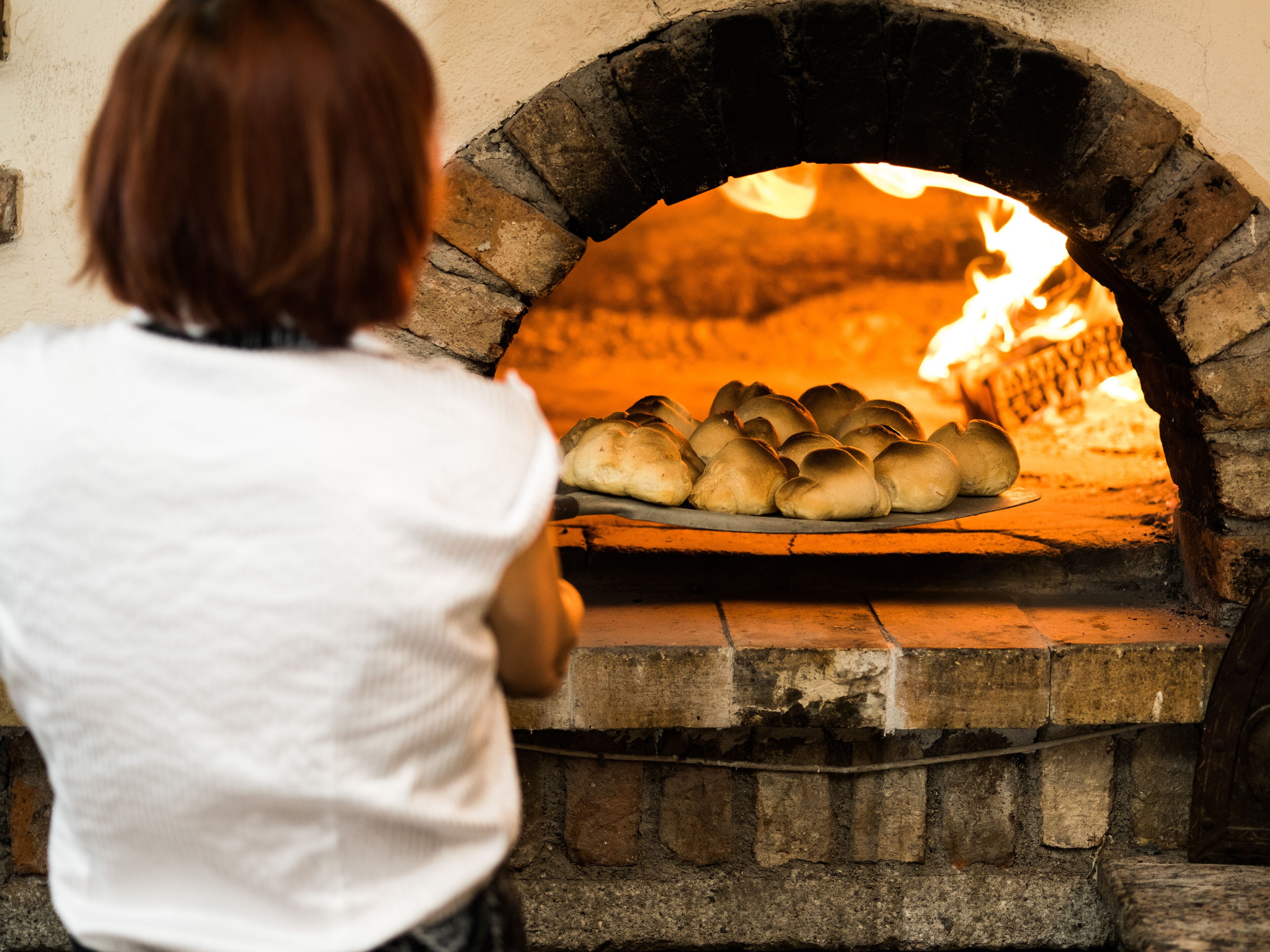 A person in front of a brick oven with bread baking inside.