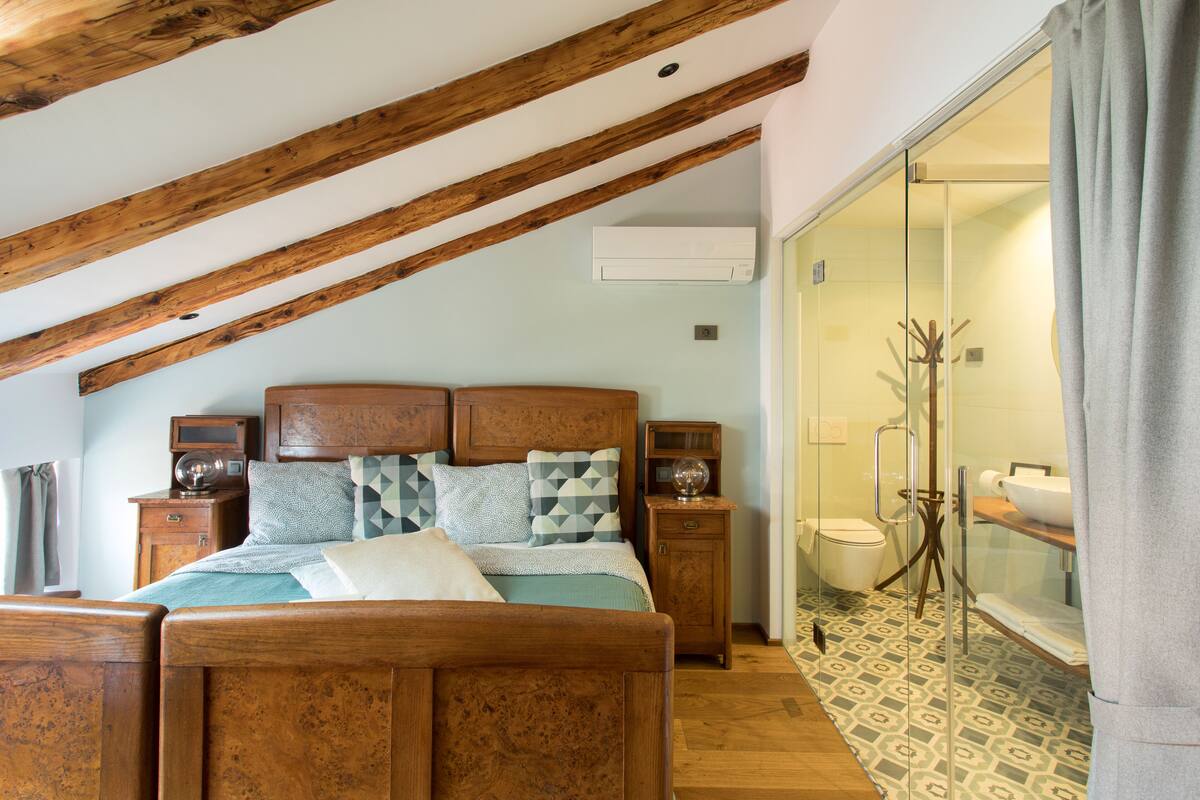 A bedroom with a wooden bed, a nightstand, a dresser, and a bathroom with a glass shower door.