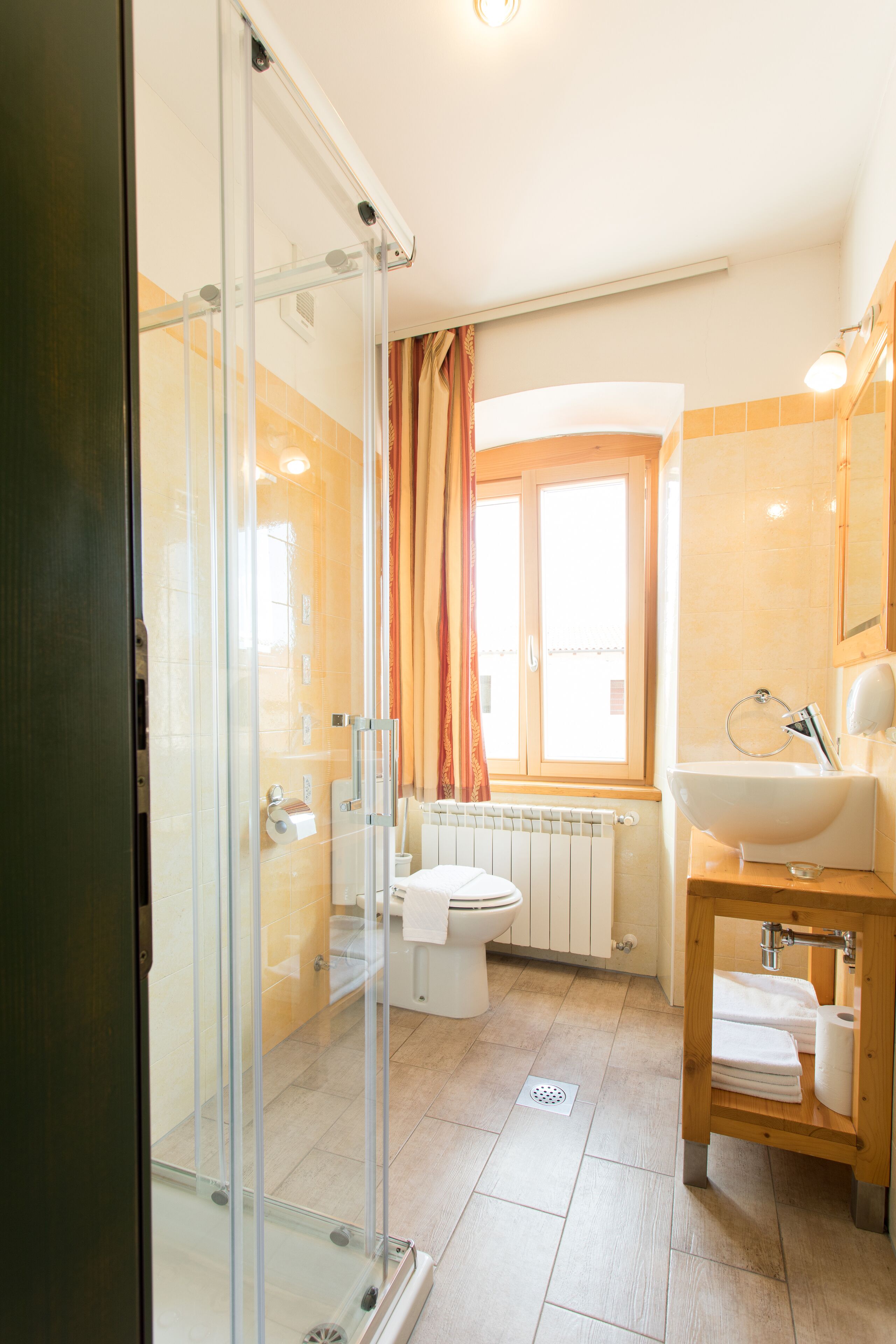Un bany modern amb una cabina de dutxa de vidre, un vàter, un rentapans i una finestra amb cortines.
