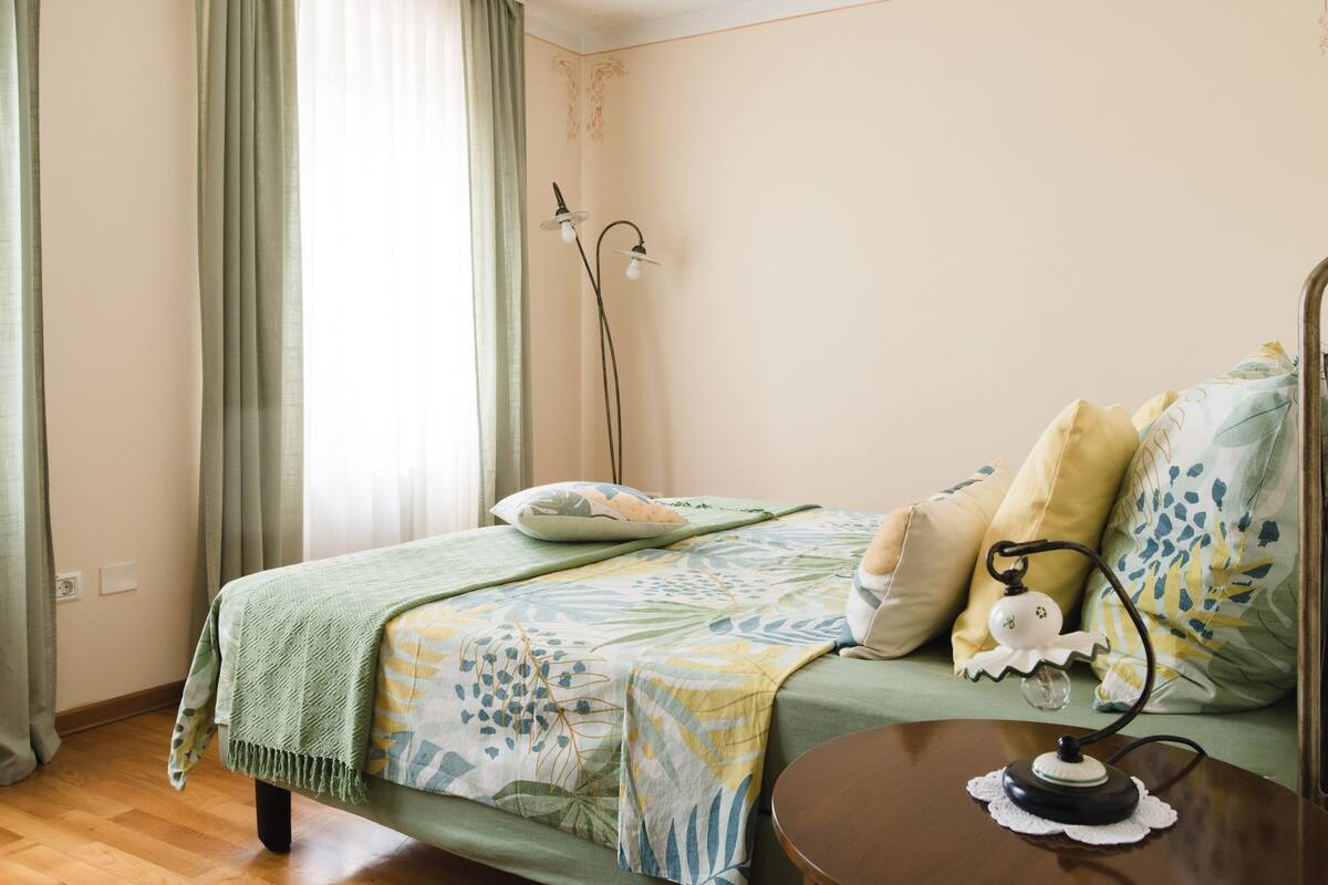 A bedroom with a bed, a bedside table, a lamp, and a window with curtains.