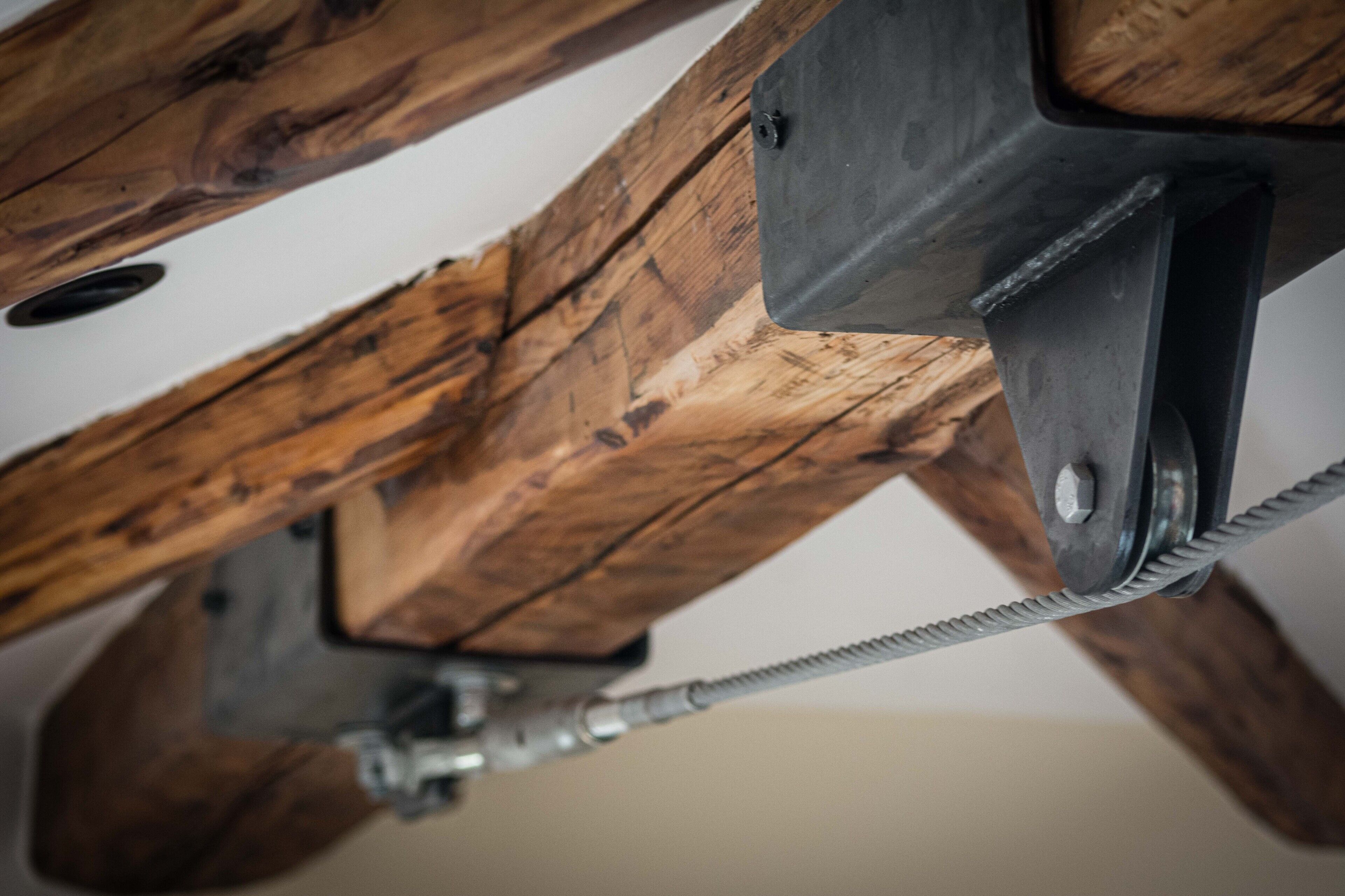 Un ventilador de techo con estructura de viga de madera y componentes metálicos.