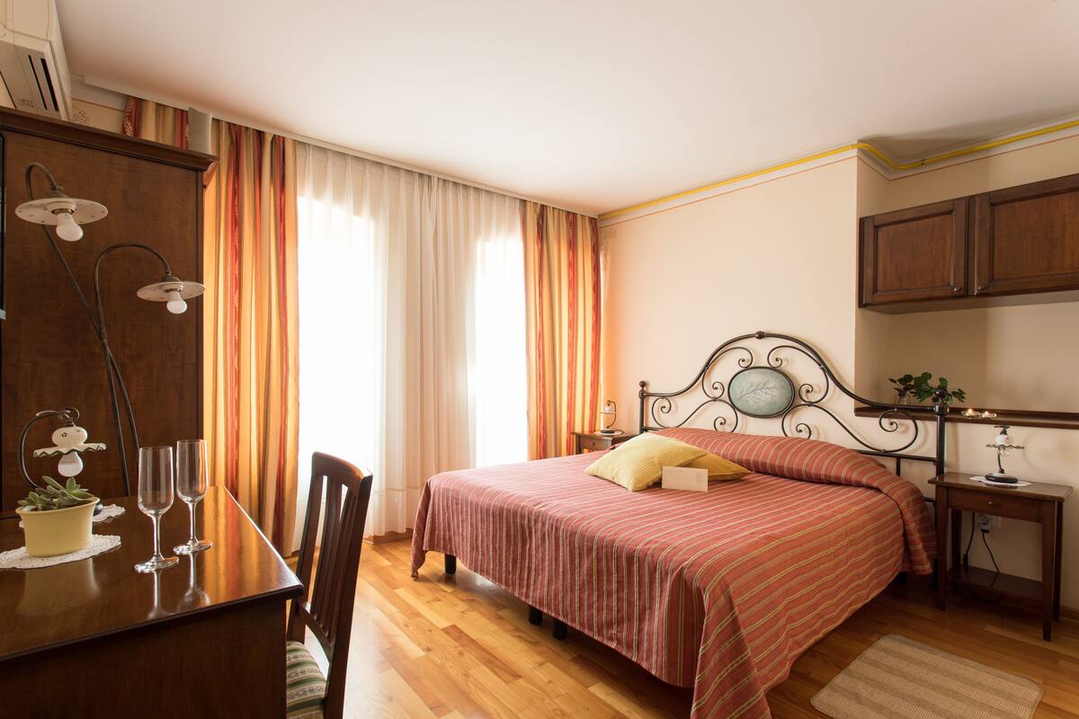 A bedroom with a bed, bedside table, lamp, curtains, and a wooden dresser.