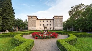 A historic building with a symmetrical facade, a central fountain, and a well-manicured garden with hedges and red flowers. - Špacapanova hiša (Komen)